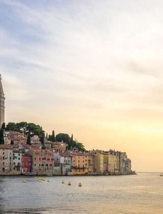 Ville côtière aux maisons colorées et clocher près de la mer, vue au coucher du soleil depuis un glamping.