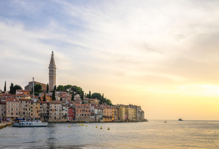 Ciudad costera con casas coloridas y torre de iglesia al borde del mar, vista al atardecer desde glamping.