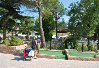 Familia jugando minigolf en Altomincio Family Park, Lombardía, Italia, con piscina y árboles al fondo.