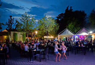 Sera al Altomincio Family Park in Lombardia, con famiglie a cena, bambini che giocano e luci soffuse.