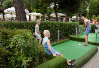 Famille jouant au mini-golf au parc Altomincio Family en Lombardie, Italie, entourée de verdure et de parasols.