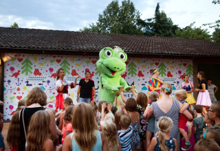 Børn samles foran en scene med en grøn maskot og voksne i kostumer i Altomincio Family Park, Lombardiet.