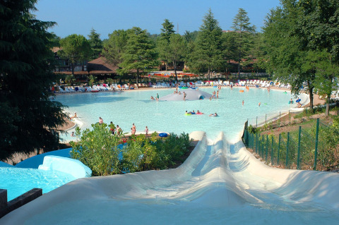 Toboganes de agua desembocan en una piscina familiar grande rodeada de tumbonas y árboles en Altomincio Family Park.