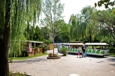 Parco vacanze in Lombardia con famiglie sul trenino turistico verde tra alberi e casette di legno.