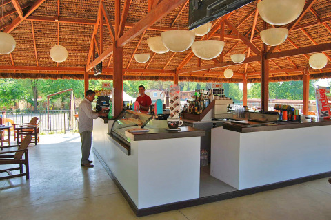 Buitenbar in het Altomincio Family Park in Lombardije, Italië, met bezoekers en barmannen onder een rieten dak.