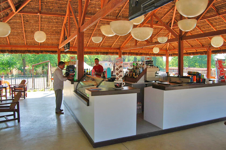Open-air bar at Altomincio Family Park in Lombardy, Italy, with guests and bartenders under a thatched roof.