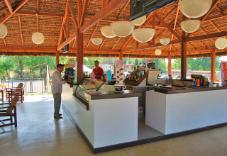 Bar en plein air au Altomincio Family Park en Lombardie, Italie, avec clients et serveurs sous un toit en chaume.