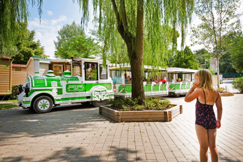 Una niña en bañador observa un tren turístico verde y blanco en Altomincio Family Park, Lombardía, Italia.