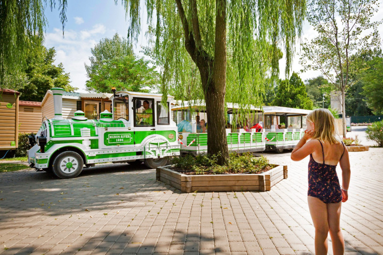 A child in a swimsuit looks at a green and white tourist train at Altomincio Family Park in Lombardy, Italy.
