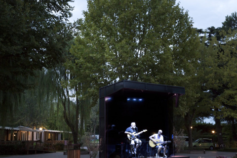 Concerto all'aperto all'Altomincio Family Park in Lombardia, Italia, musicisti si esibiscono sul palco al tramonto.
