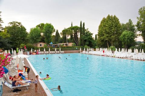 Piscina al aire libre con personas nadando y descansando, rodeada de árboles y tumbonas en Altomincio Family Park.
