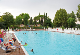 Piscina al aire libre con personas nadando y descansando, rodeada de árboles y tumbonas en Altomincio Family Park.
