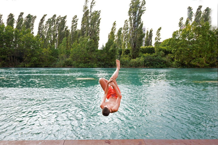 A boy jumps into the water at Altomincio Family Park in Lombardy, Italy, surrounded by lush green trees.