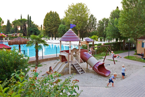Niños jugando en un parque infantil con tobogán y columpios junto a una piscina en Altomincio Family Park, Lombardía.