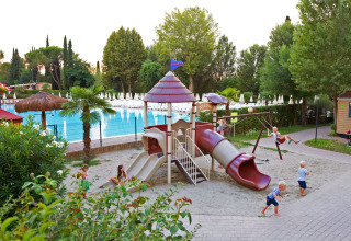 Kinderen spelen op een speeltuin met glijbaan en schommels aan het zwembad in Altomincio Family Park, Lombardije.