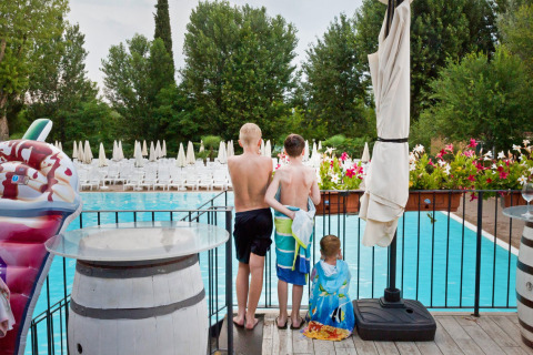 Three children with towels look out over a swimming pool at Altomincio Family Park in Lombardy, Italy.