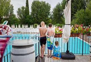 Trois enfants avec des serviettes regardent la piscine du parc Altomincio Family Park en Lombardie, Italie.