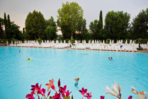 Udendørs swimmingpool i Altomincio Family Park, Lombardiet, Italien, med solsenge og parasoller.