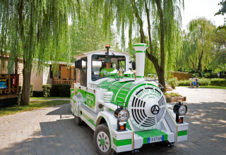 A green and white tourist train drives through Altomincio Family Park, surrounded by trees in Lombardy, Italy.