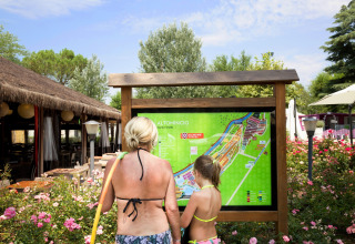 Two people in swimwear look at a map of Altomincio Family Park, surrounded by flowers and greenery.