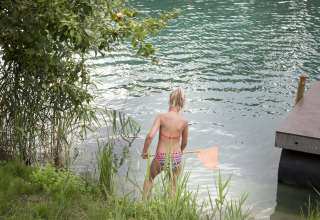 Child in swimsuit with fishing net by lake at Altomincio Family Park, Lombardy, Italy, on a summer day.