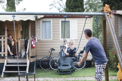 A man pushes a child on a swing in front of a mobile home as a woman sits on the porch at a holiday park.