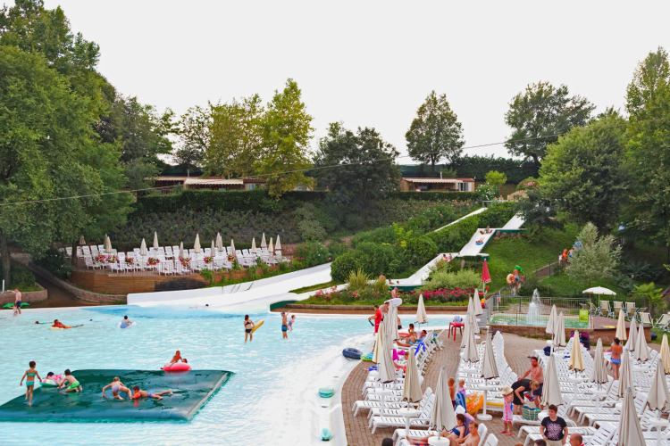 Swimming pool and water slides at Altomincio Family Park in Italy, with guests relaxing on sun loungers.