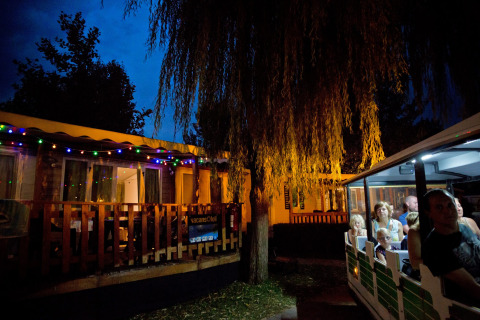 Vista nocturna en Altomincio Family Park, Lombardía, Italia, con cabañas y visitantes en un tren turístico.