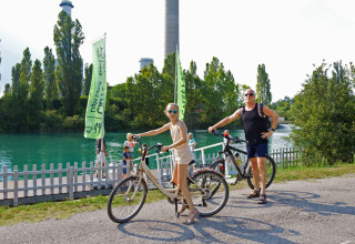 Two people with bicycles stopping by a scenic riverside in Altomincio Family Park, Lombardy, Italy.
