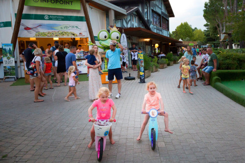 Children riding bikes in front of the info point at Altomincio Family Park, Lombardy, Italy with families.