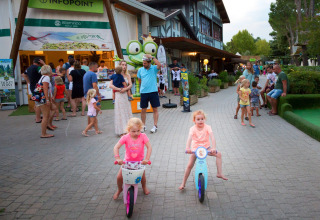 Børn cykler foran informationspunktet i Altomincio Family Park, Lombardiet, Italien, fyldt med familier.