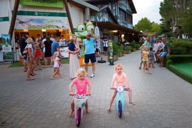 Children riding bikes in front of the info point at Altomincio Family Park, Lombardy, Italy with families.