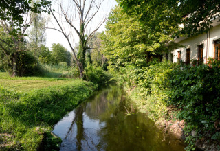 Tranquil stream at Altomincio Family Park in Lombardy, Italy, bordered by lush greenery and a building.