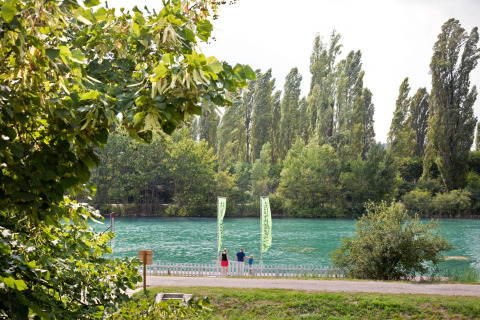 Groene bomen en een helderblauwe rivier bij Altomincio Family Park in Lombardije, Italië, met mensen langs de oever.