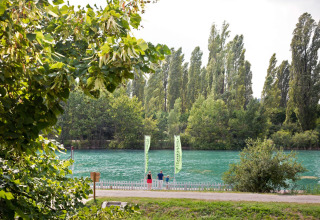 Groene bomen en een helderblauwe rivier bij Altomincio Family Park in Lombardije, Italië, met mensen langs de oever.
