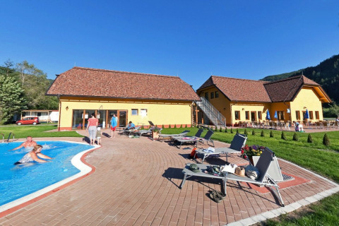Camping Bella Austria nel parco vacanze in Stiria, Austria, con edifici gialli, piscina, lettini e ospiti rilassati.