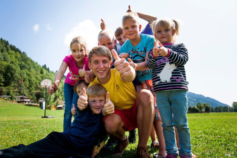 Gruppo di bambini sorridenti e un adulto fanno pollice in su al Camping Bella Austria in Stiria, Austria.