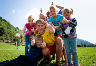 Gruppo di bambini sorridenti e un adulto fanno pollice in su al Camping Bella Austria in Stiria, Austria.