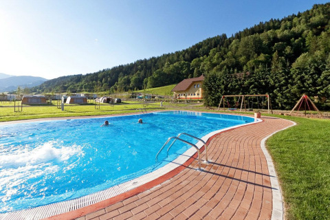 Piscina al aire libre y zona de juegos en Camping Bella Austria, rodeado de colinas verdes en Estiria.