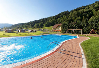 Outdoor swimming pool and playground at Camping Bella Austria holiday park in Styria, Austria, with hills.