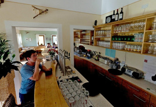 Uomo che beve al bar del Camping Bella Austria in Stiria, Austria, con bicchieri e bottiglie sugli scaffali.