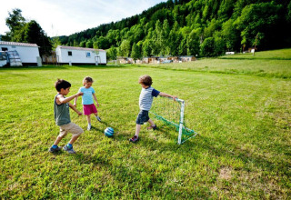 Børn leger fodbold på en grøn mark ved Camping Bella Austria-feriepark i Stiermarken, Østrig.