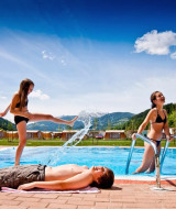 Children playing by the pool with mountains in the background at Camping Bella Austria holiday park.