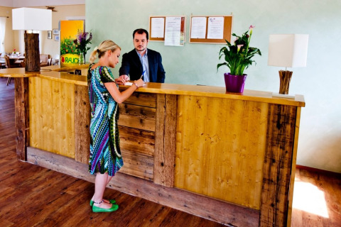 Receptionist e ospite al bancone di legno al Camping Bella Austria, parco vacanze in Stiermarken, Austria.