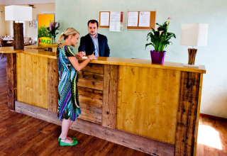 Receptionist en gast bij houten balie in Camping Bella Austria vakantiepark, Stiermarken, Oostenrijk.