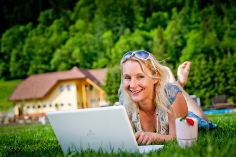 Mujer relajándose sobre el césped con un portátil en Camping Bella Austria, un parque vacacional en Estiria, Austria.