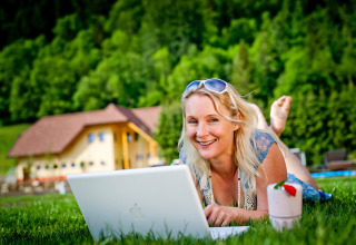 Donna che si rilassa sull’erba con un laptop al Camping Bella Austria, parco vacanze in Stiria, Austria.
