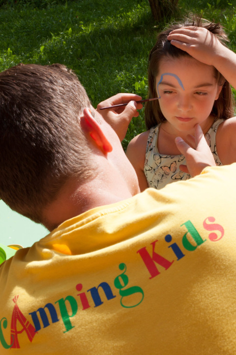 Uomo dipinge il viso di una bambina all'aperto al parco vacanze Camping Bella Austria, Stiria, Austria.