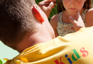 Uomo dipinge il viso di una bambina all'aperto al parco vacanze Camping Bella Austria, Stiria, Austria.