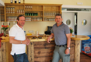 Due uomini al bancone del bar presso Camping Bella Austria, Stiria, Austria, circondati da bicchieri e bevande.